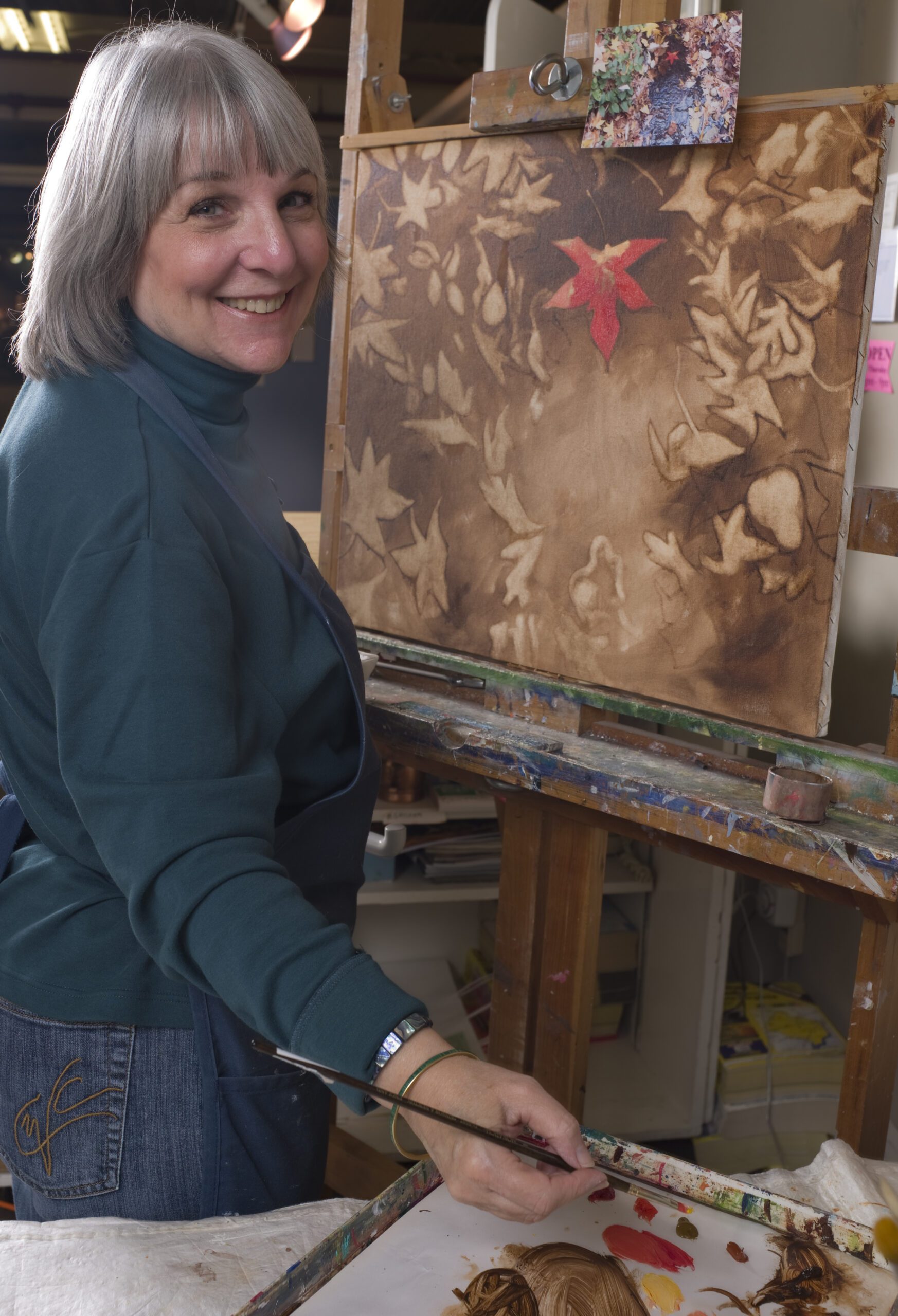 Woman smiling while holding a brush with a canvass on her side