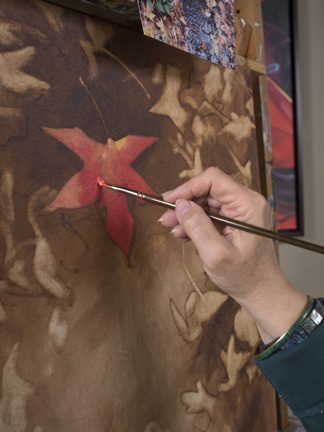 A woman holding a brush painting a leaf